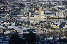 Foto einer Stadt, die an einem Fluss liegt, über die eine Straßenbrücke führt.