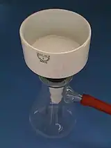 Büchner-Trichter mit eingelegtem runden Filterpapier auf einer Saugflasche mit angeschlossenem Vakuumschlauch