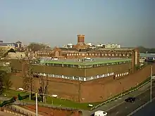 Das Gefängnis in Reading von schräg oben aufgenommen; Gebäudekomplex mit einer umgebenden Backsteinmauer. Im Vordergrund eine Straße mit Autos, im Hintergrund Hochhäuser.