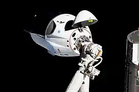 Crew Dragon im Anflug an die ISS; im Vordergrund der (nicht verwendete) Canadarm2
